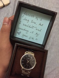 a person holding a watch in their hand with a note written on the box next to it