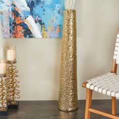 a tall gold vase sitting next to a white chair