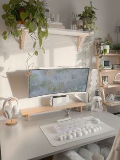 a desk with a computer, keyboard and plant on it in front of a window