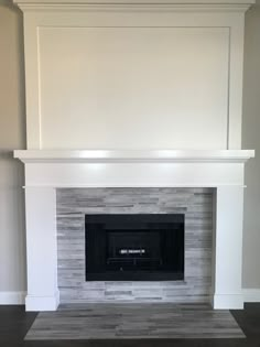 an empty fireplace with white paint and wood flooring in a room that is painted gray