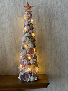 a christmas tree made out of seashells and lights on a shelf in front of a wall