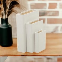 three white vases sitting next to each other on top of a wooden table in front of a brick wall