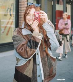 a woman is taking a photo with her cell phone on the street while wearing sunglasses