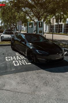 a black car is parked in the parking lot next to an electric charging station and gas pumps