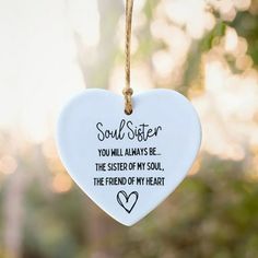 a white ceramic heart hanging from a string with the words soul sister on it, and two hearts at the bottom