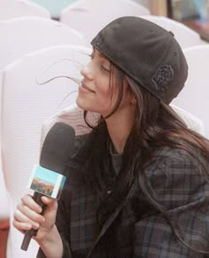 a woman sitting in a chair holding a microphone and wearing a black hat while talking on the phone