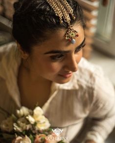 a woman in a white shirt holding a bouquet and wearing a gold head piece with jewels on it