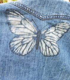 a white butterfly painted on the back of a blue jean jacket with holes in it