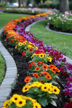 colorful flowers line the edge of a brick garden edging in front of a lawn