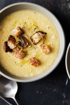 there is a bowl of soup with meat and cheese in it next to two spoons