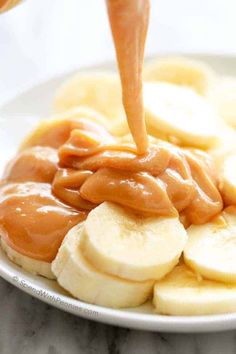 a plate with bananas and peanut butter is being drizzled on top by a spoon