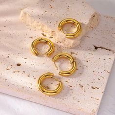 three pairs of gold - plated hoop earrings on top of a piece of paper