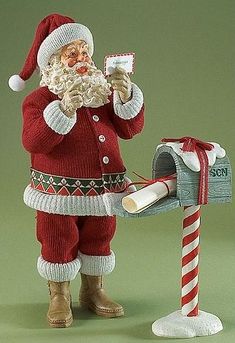 a santa claus mailbox with a candy cane in his hand and an ornament next to it