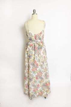 "Vintage 1970s boho maxi dress. Off white, pastel floral and paisley pattern cotton. Spaghetti strap, lace tom wide neckline. Unique billowy top over a fitted bodice with decorative buttons and knife pleats with has a wrap around tie. Full length straight skirt. Hidden back nylon zipper. Lined in off white semi-sheer cotton. Label: S.Howard Hirsh Fits like size: Smal l- See measurements to be sure. Measurements: Bust: 35\" Waist: 31\" - can be tied tighter if desired Hip: 38\" Length: 52\" Condi Lace Toms, Nude Slip Dress, Vintage Dresses 1960s, 1970s Dresses, 1980s Dresses, 1960's Dress, Boho Maxi, Cotton Maxi, House Dress