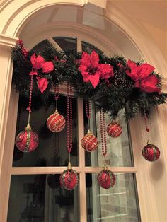 a window decorated with red ornaments and poinsettia hanging from it's side