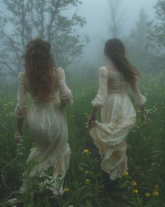 two women in dresses are walking through the foggy field with yellow wildflowers