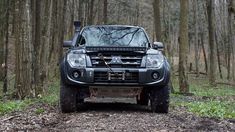 the front end of a four - door pick up truck on a dirt road in the woods