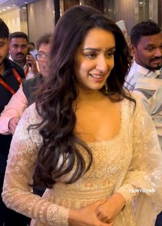 a woman in a white dress standing next to other people and looking at the camera