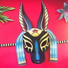 an egyptian mask on a red wall with flowers in the backgroung area