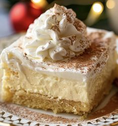 a piece of cake with whipped cream on top sits on a plate next to a christmas tree