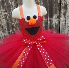 a red dress with white polka dots and an orange sesame character on the front, in front of a wooden fence