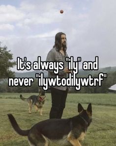 a man with long hair and beard standing in the grass next to two german shepherd dogs