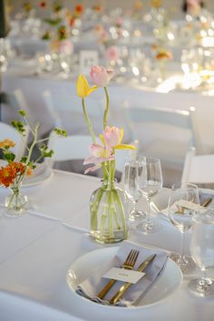 the table is set with white linens, silverware and flowers in vases