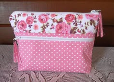 a pink and white polka dot purse with flowers on the front, sitting on a lace tablecloth