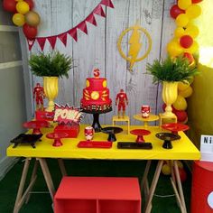 a yellow table topped with red and yellow cake next to a wall covered in balloons