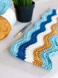 a crochet afghan next to a ball of yarn and a potted plant