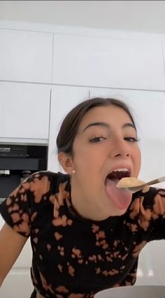 a woman with her mouth open and holding a spoon in her hand while eating food