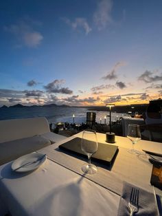 the table is set with two wine glasses and plates on it, overlooking the ocean