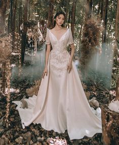 a woman standing in the woods wearing a wedding dress