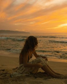 a woman sitting on top of a sandy beach next to the ocean under a cloudy sky