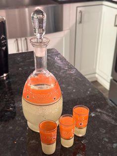 an orange glass decanter and four shot glasses on a kitchen counter