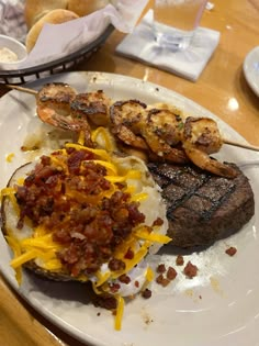 steak, potatoes and shrimp on a white plate at a table with other food items