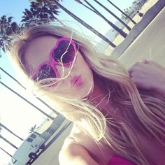 a woman wearing pink sunglasses standing next to a palm tree in front of a building