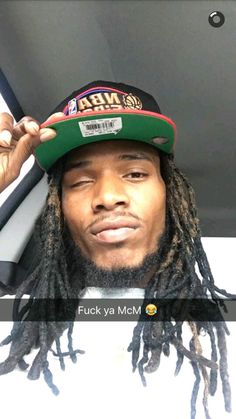 a man with dreads wearing a hat and holding up his cell phone to the camera