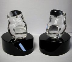 two clear glass vases sitting on top of black bases, one is shaped like a bear