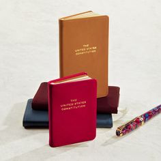 three books and a pen sitting next to each other on top of a white surface