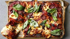 a pizza with cheese, pepperoni and spinach leaves on it sitting on top of a pan