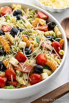 a pasta salad with tomatoes, olives and cheese in a white bowl