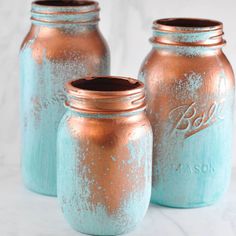 three blue and copper jars sitting on top of a white counter