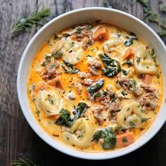 a white bowl filled with pasta and spinach on top of a wooden table next to fresh herbs