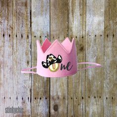 a pink hat with a black bow and one eye on it is hanging from a wooden fence