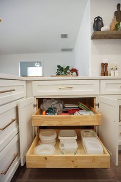 an open drawer in a kitchen with white cabinets and wooden drawers on the bottom shelf