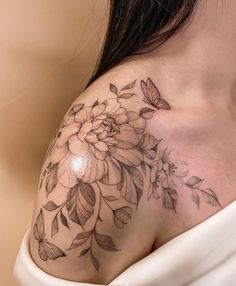 a woman's shoulder with flowers and leaves tattoo on her left side breast area