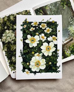 some white flowers and green leaves on top of a sheet of paper next to photos