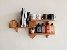 two wooden shelves with coffee mugs, books and other items on them against a white wall