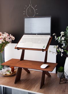 a laptop computer sitting on top of a wooden stand next to a vase with flowers